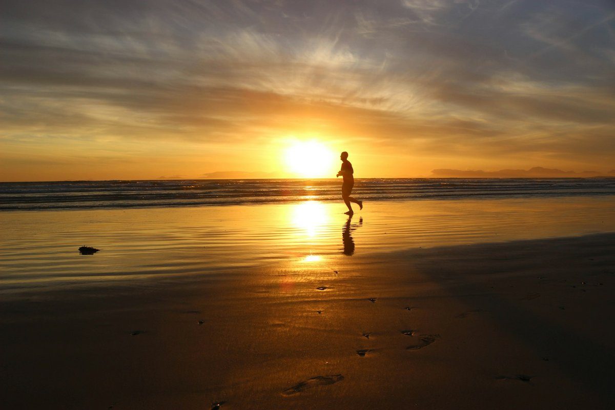 Silhouette d'un coureur sur une plage de sable, devant un soleil bas sur l'horizon