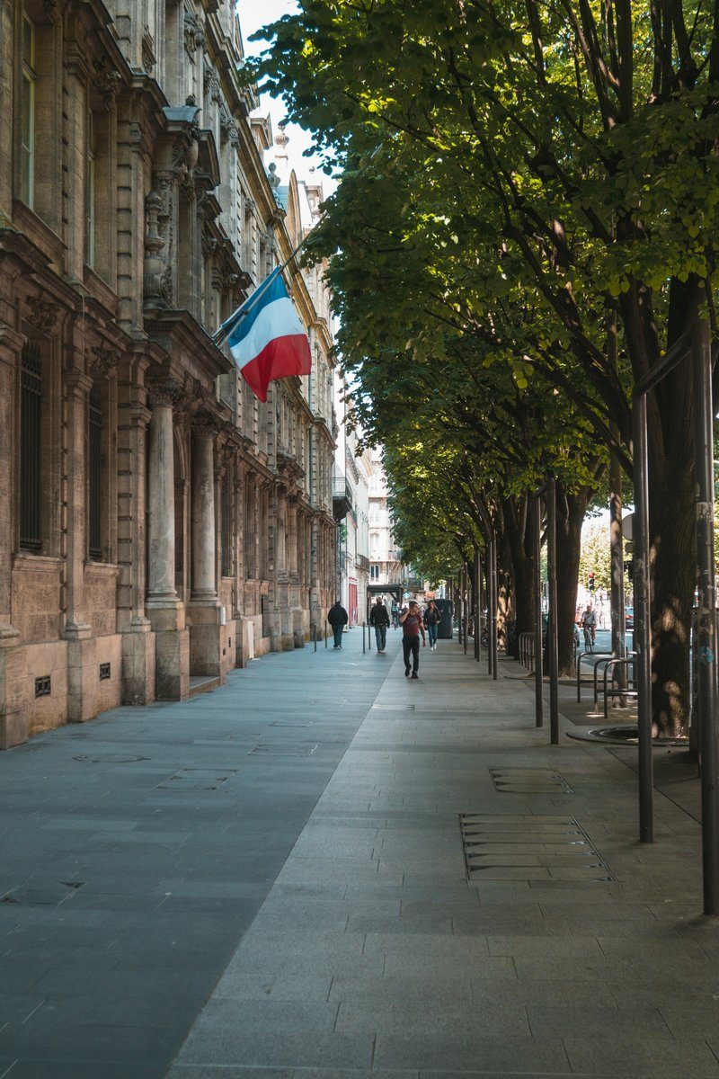 Trottoir large sous les arbres le long de façades en pierre blonde